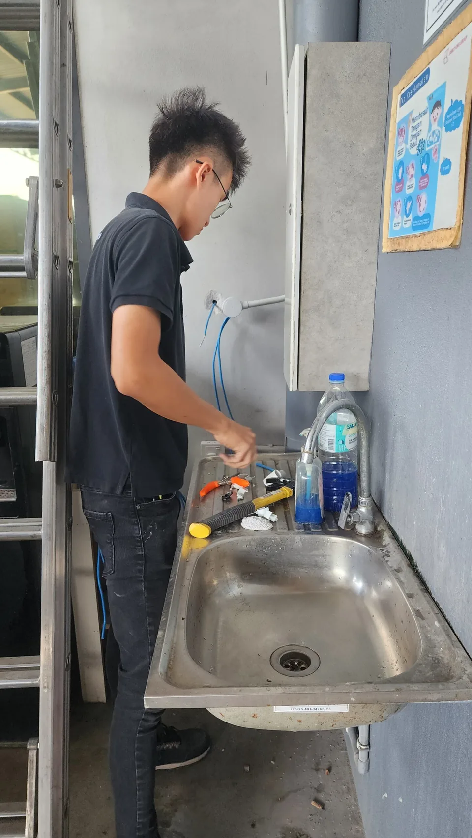 Technician preparing a wall connection beside a utility sink.