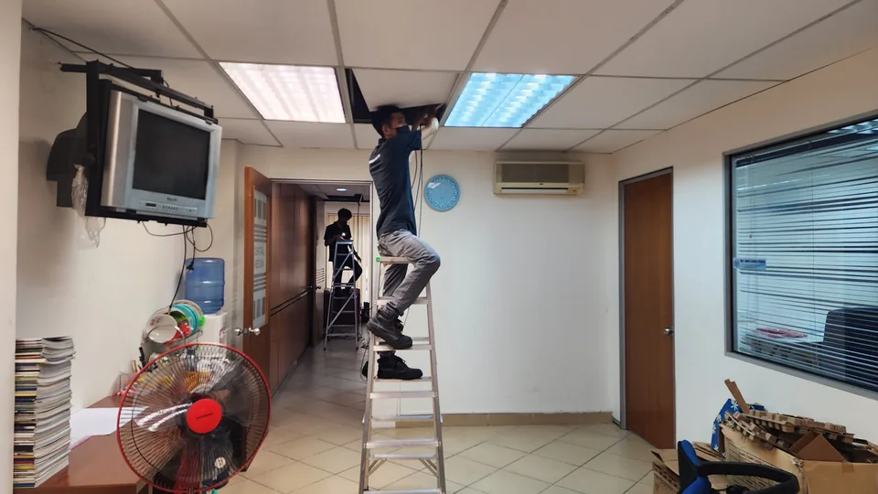 Two technicians on ladders routing cable through a suspended ceiling.
