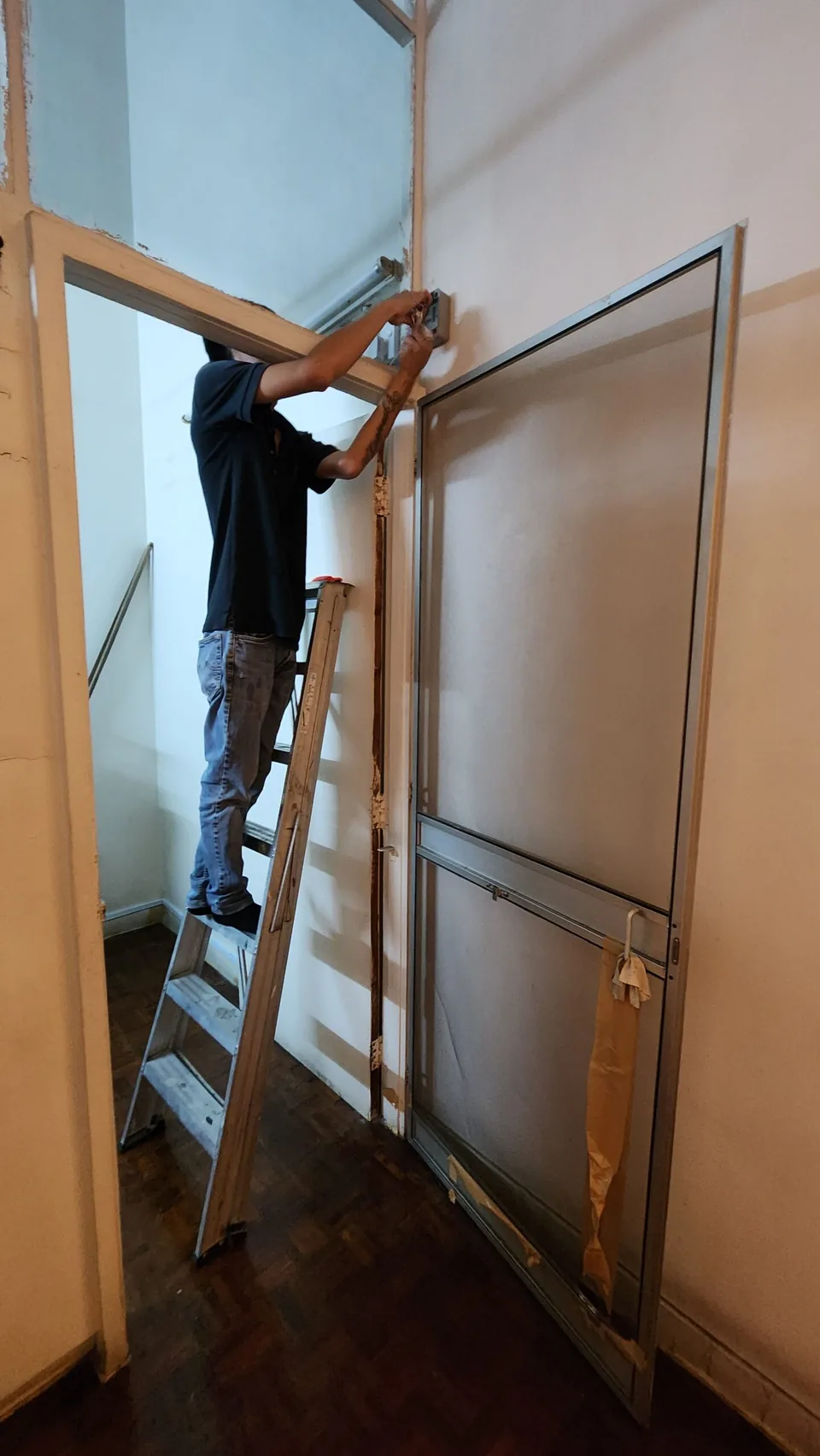 Technician on a ladder routing cable above a doorway.