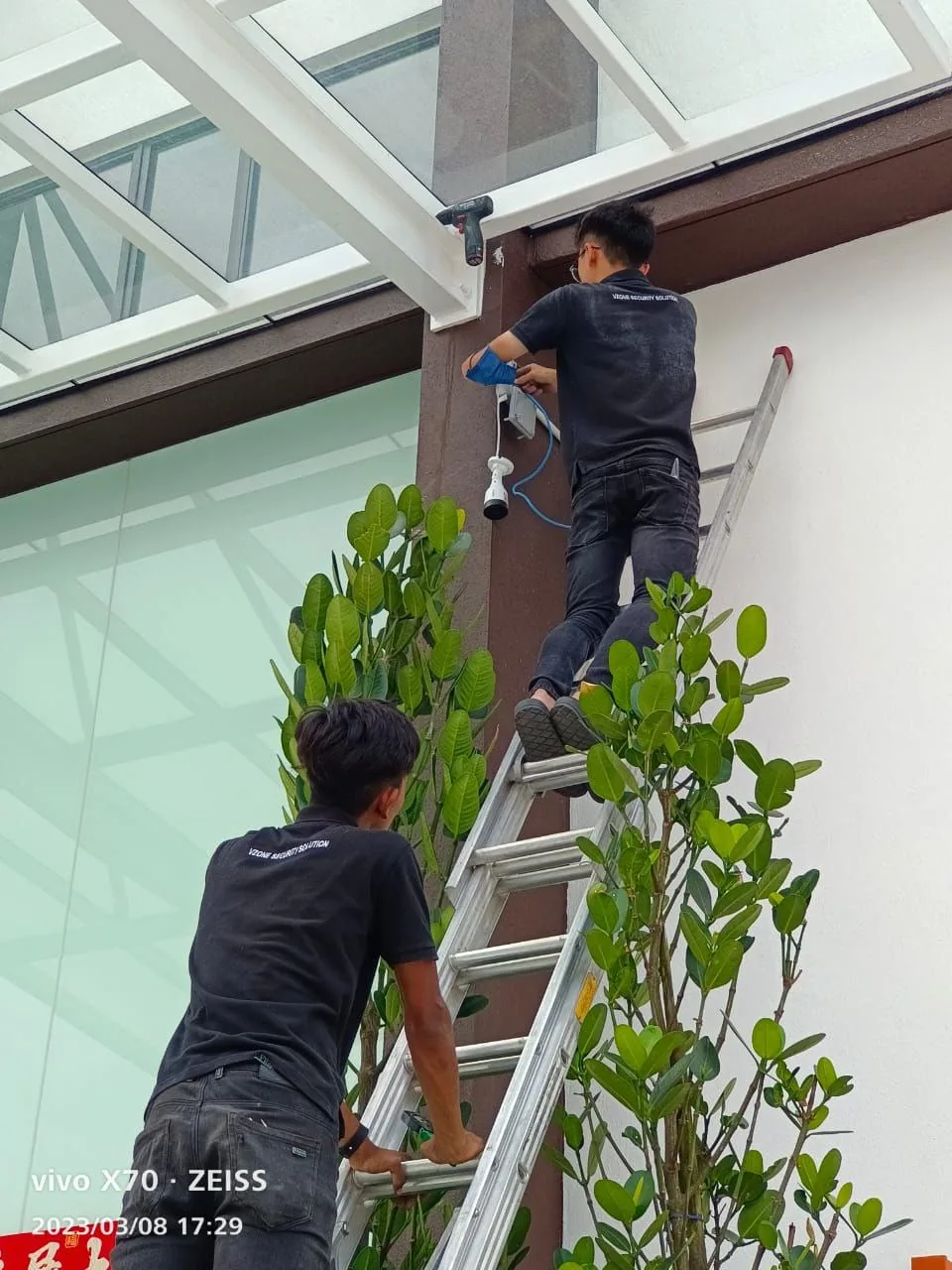 Two technicians install a device beneath an exterior canopy.