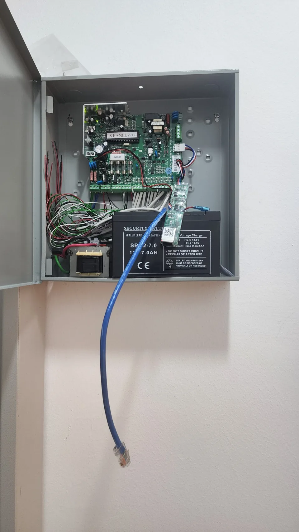 Open alarm control cabinet with circuit board and loose wiring.
