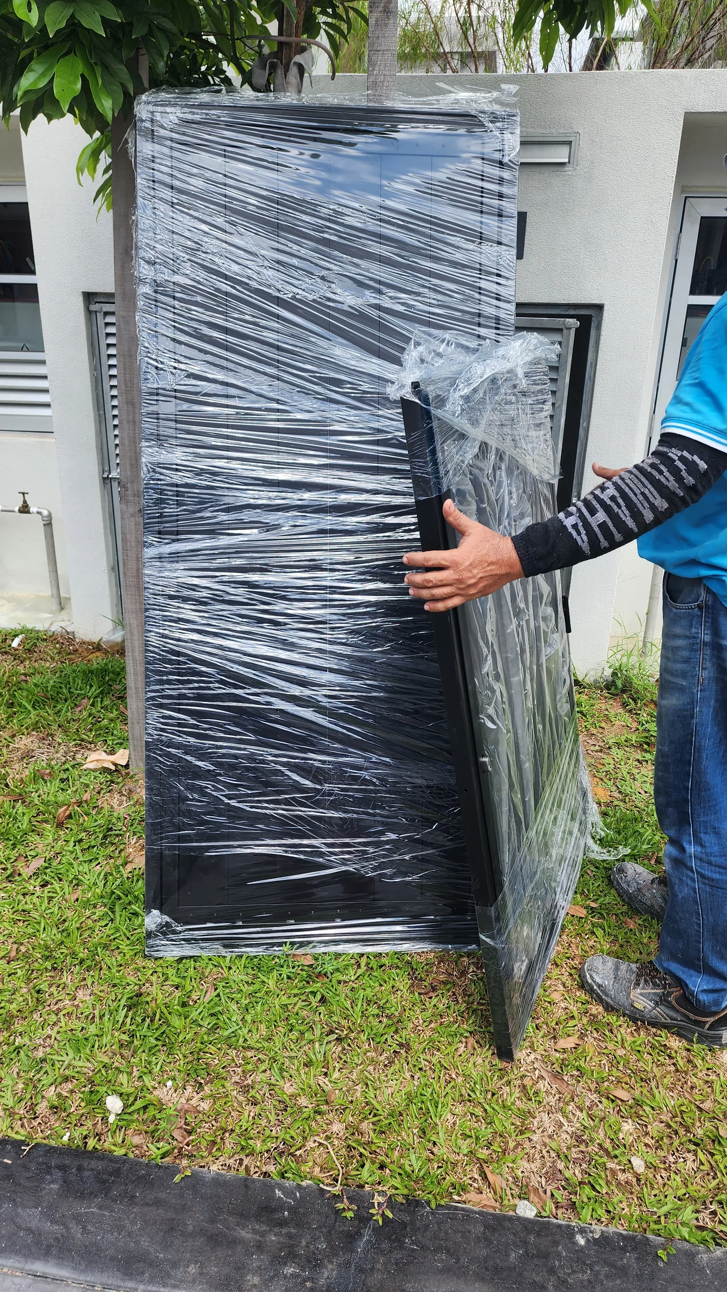 Technician steadies a plastic-wrapped metal gate panel outdoors.