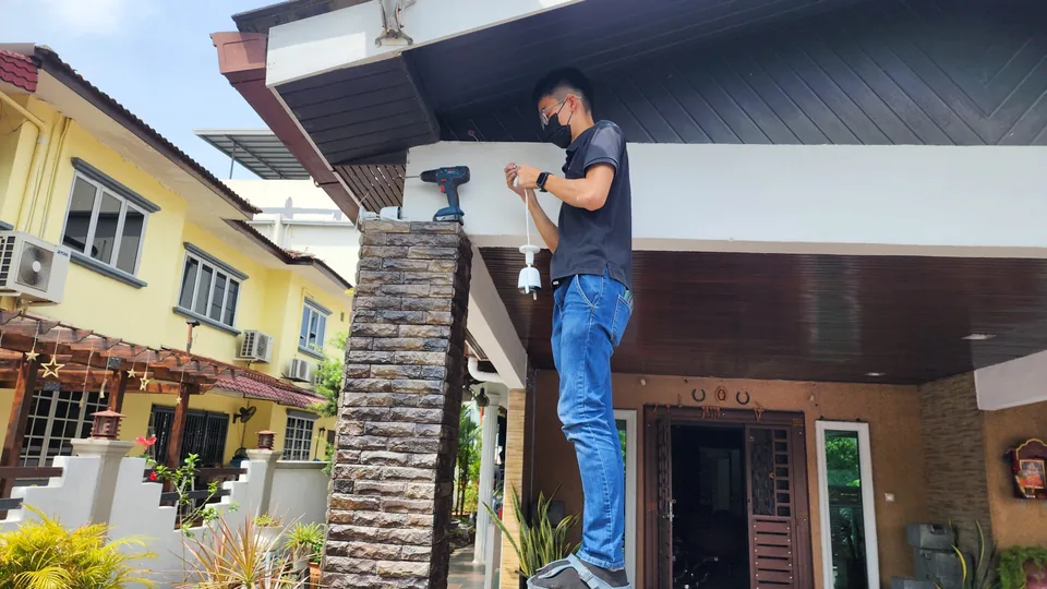 Technician on a ladder fitting a camera to a porch column.