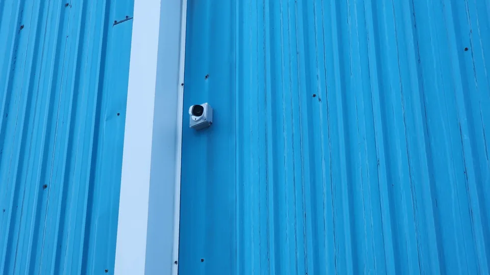 Compact camera mounted on a blue corrugated wall.