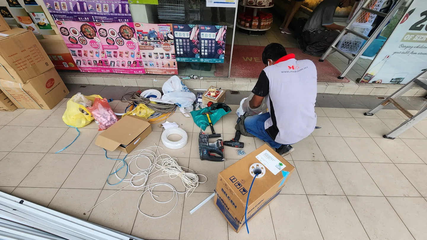 Technician prepares alarm cables and tools outside a shop entrance.