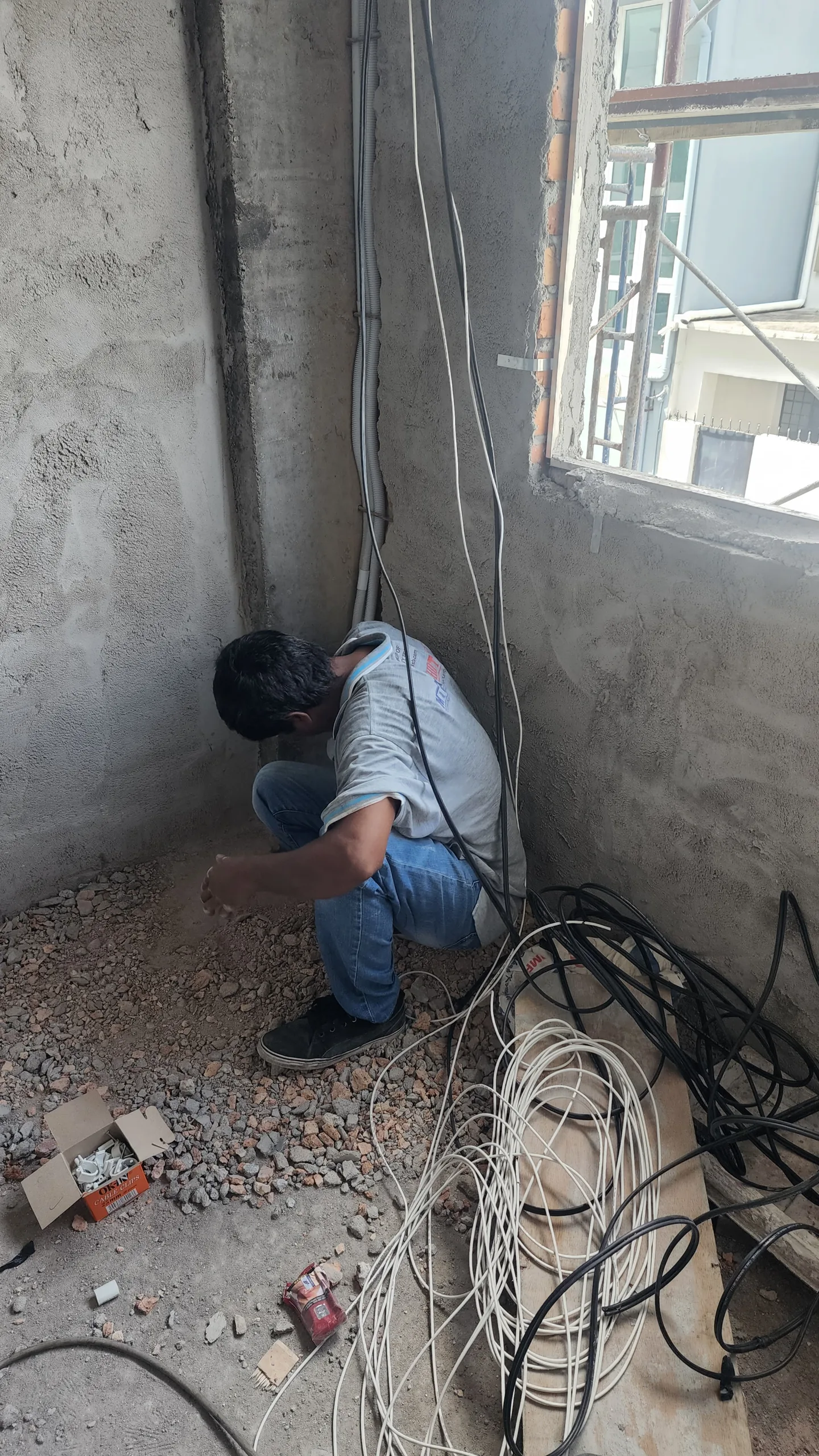 Technician kneels among cables in an unfinished room.
