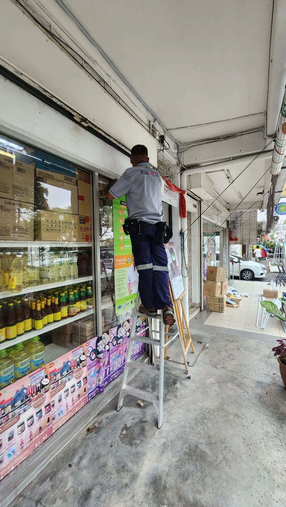Technician installs cabling above a shopfront from a ladder.