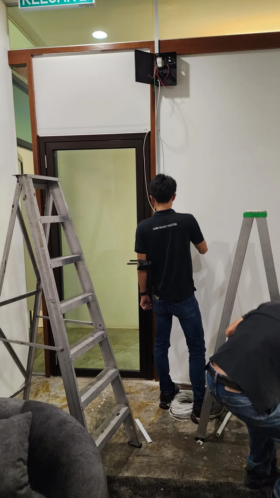 Technician inspecting overhead access hardware above a doorway.