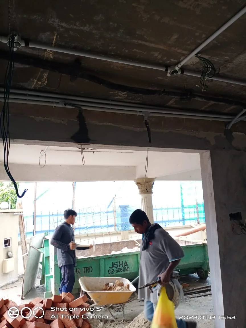 Two workers stand below ceiling conduit in a room under renovation.