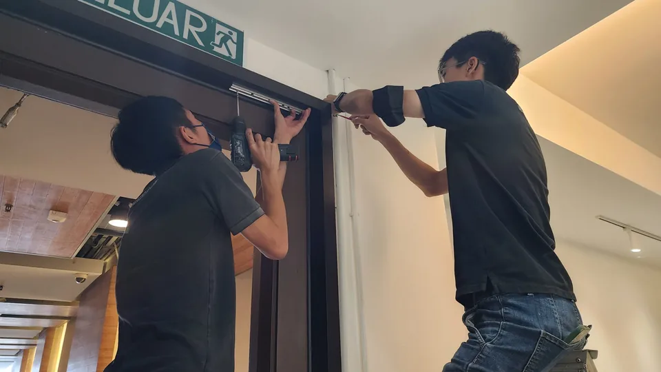 Two technicians installing a magnetic lock above a doorway.
