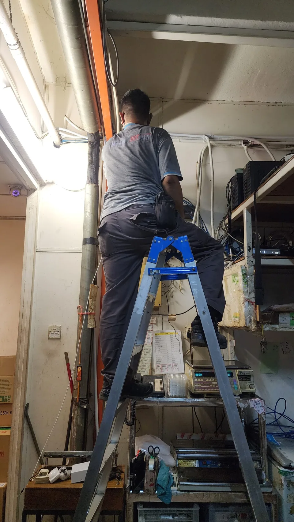 Technician works from a ladder beside exposed equipment wiring.