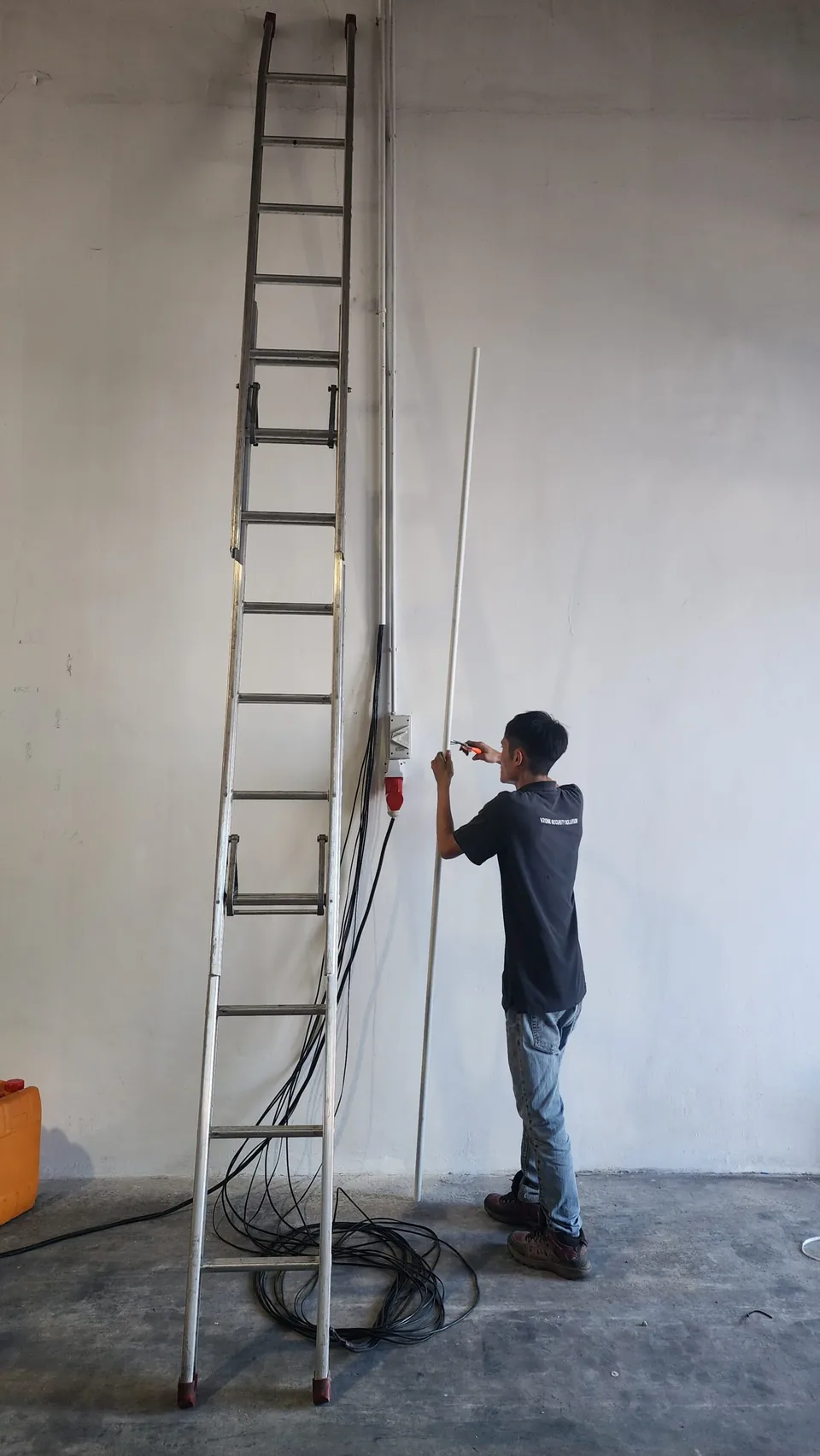 Technician works beside a tall ladder and vertical wall conduit.