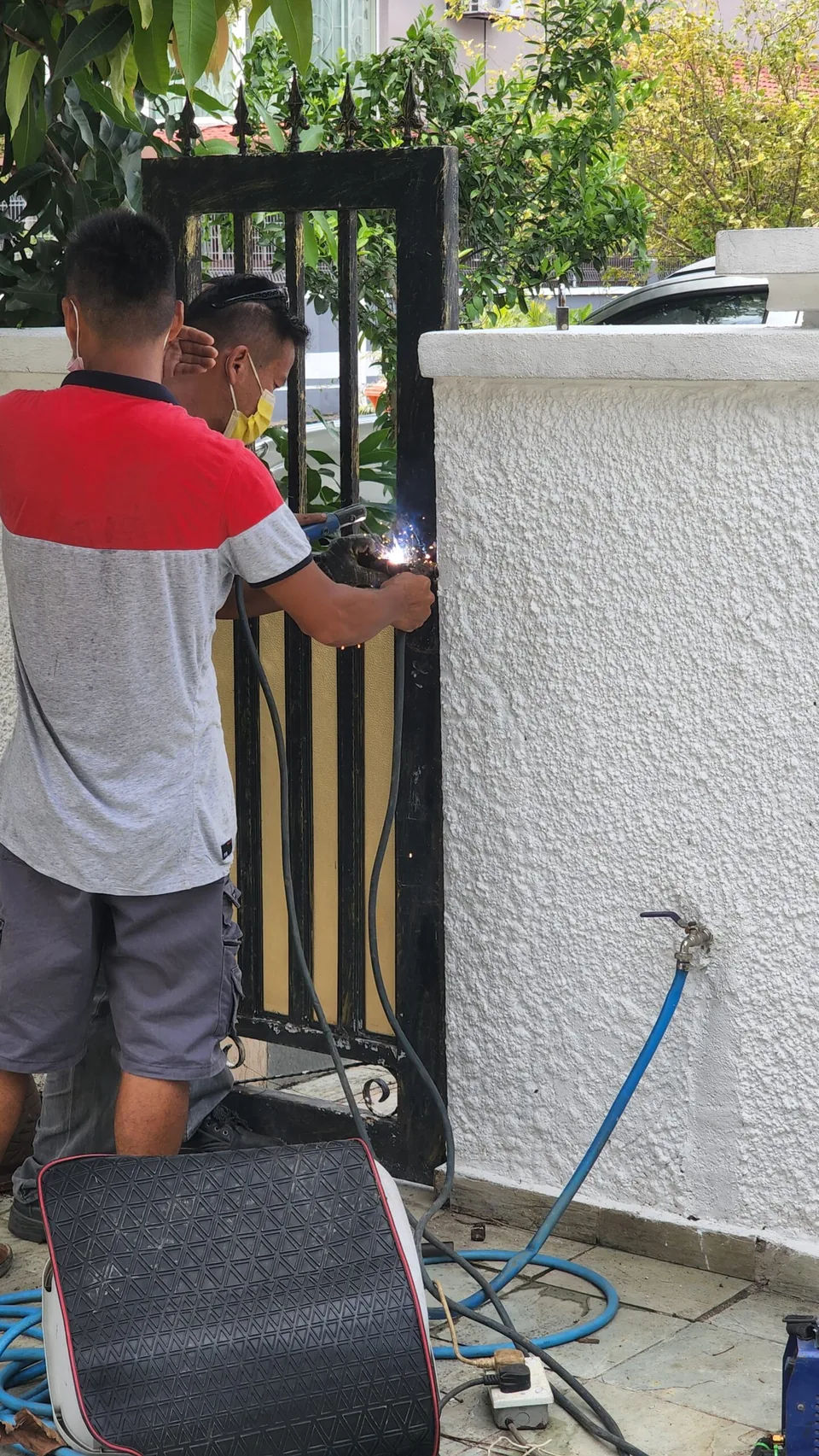 Two technicians work on gate hardware beside a boundary wall.