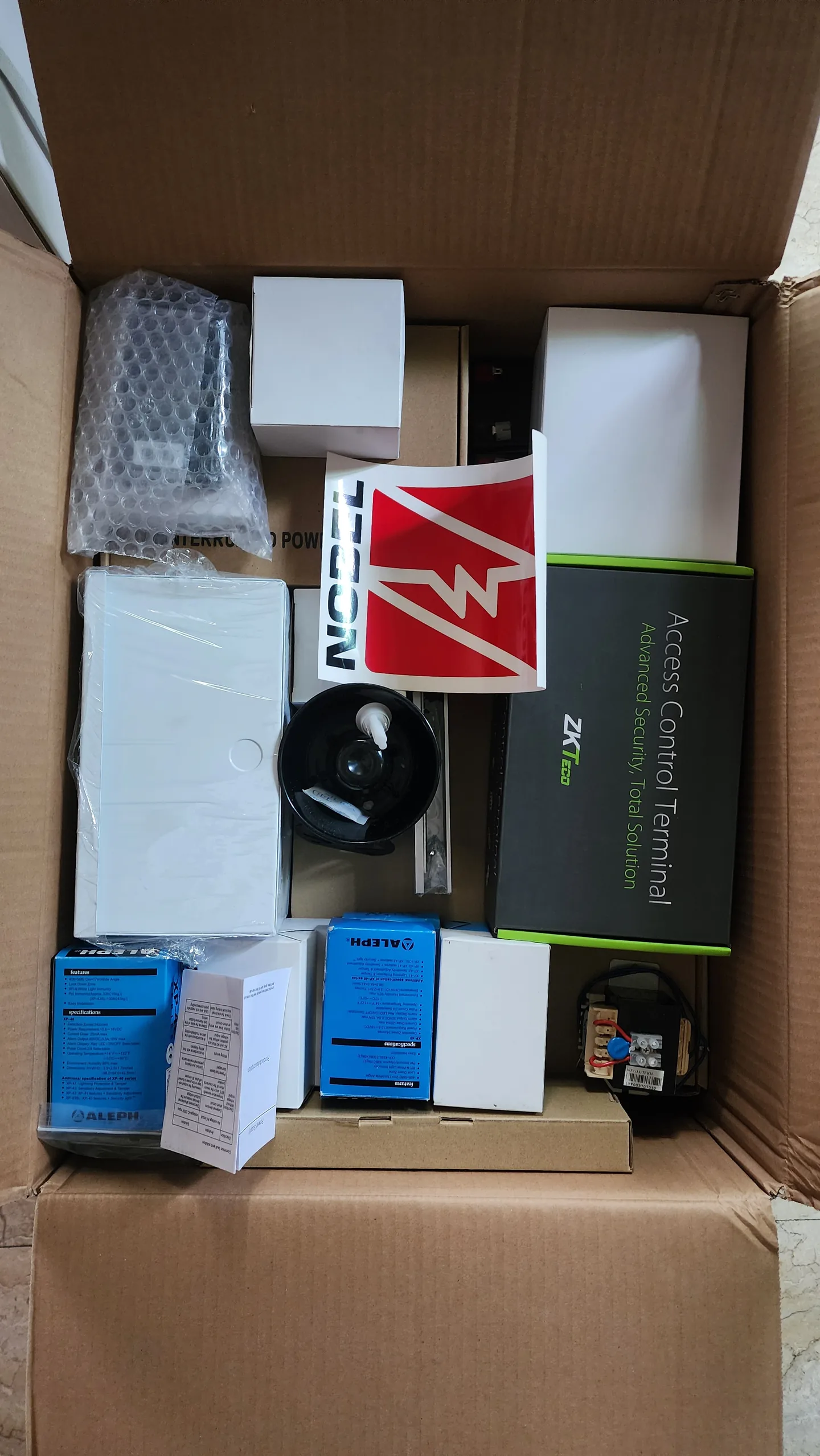 Boxed alarm control components and warning sign ready for installation.