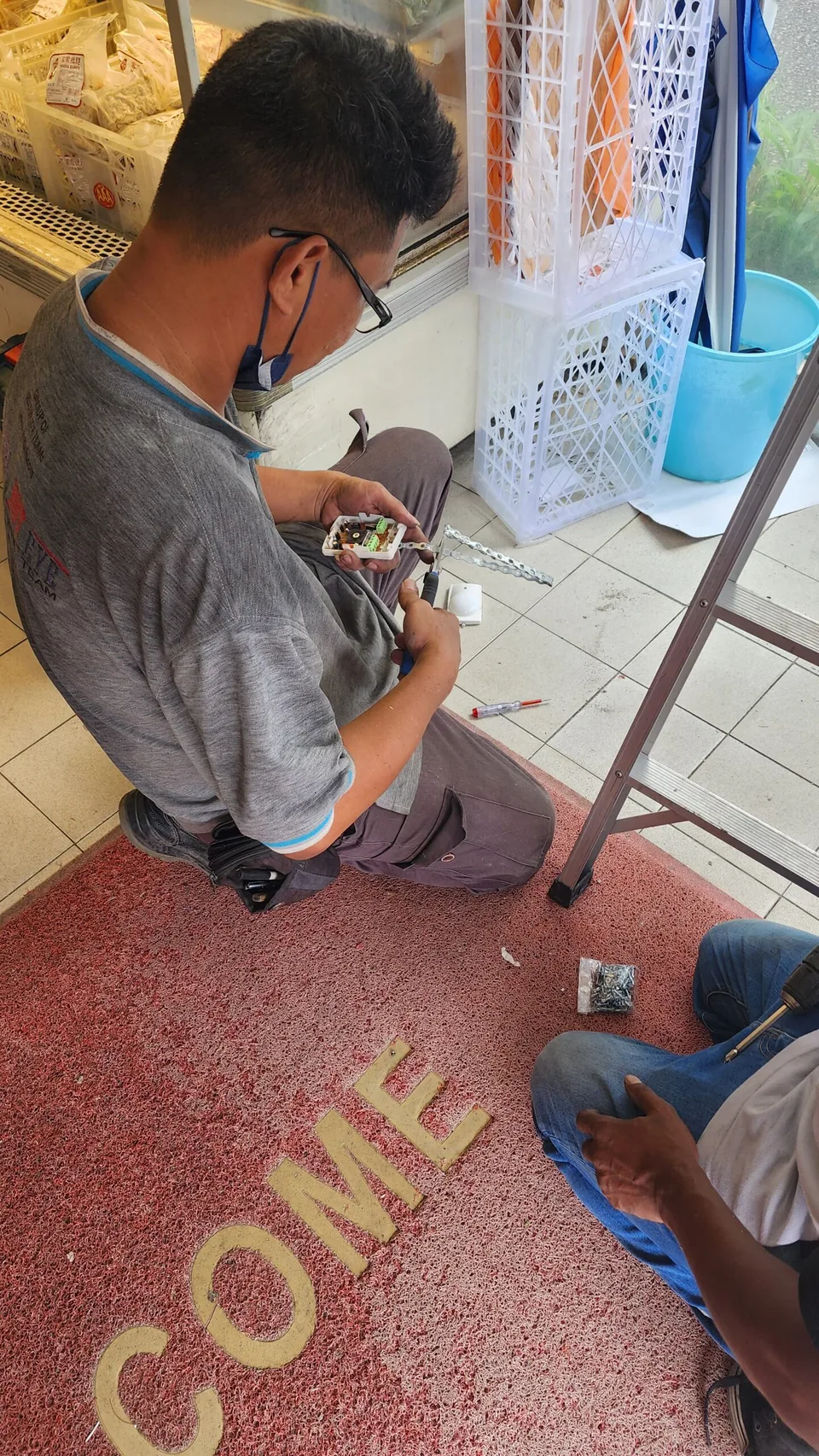 Technician assembles a small alarm component beside a ladder.
