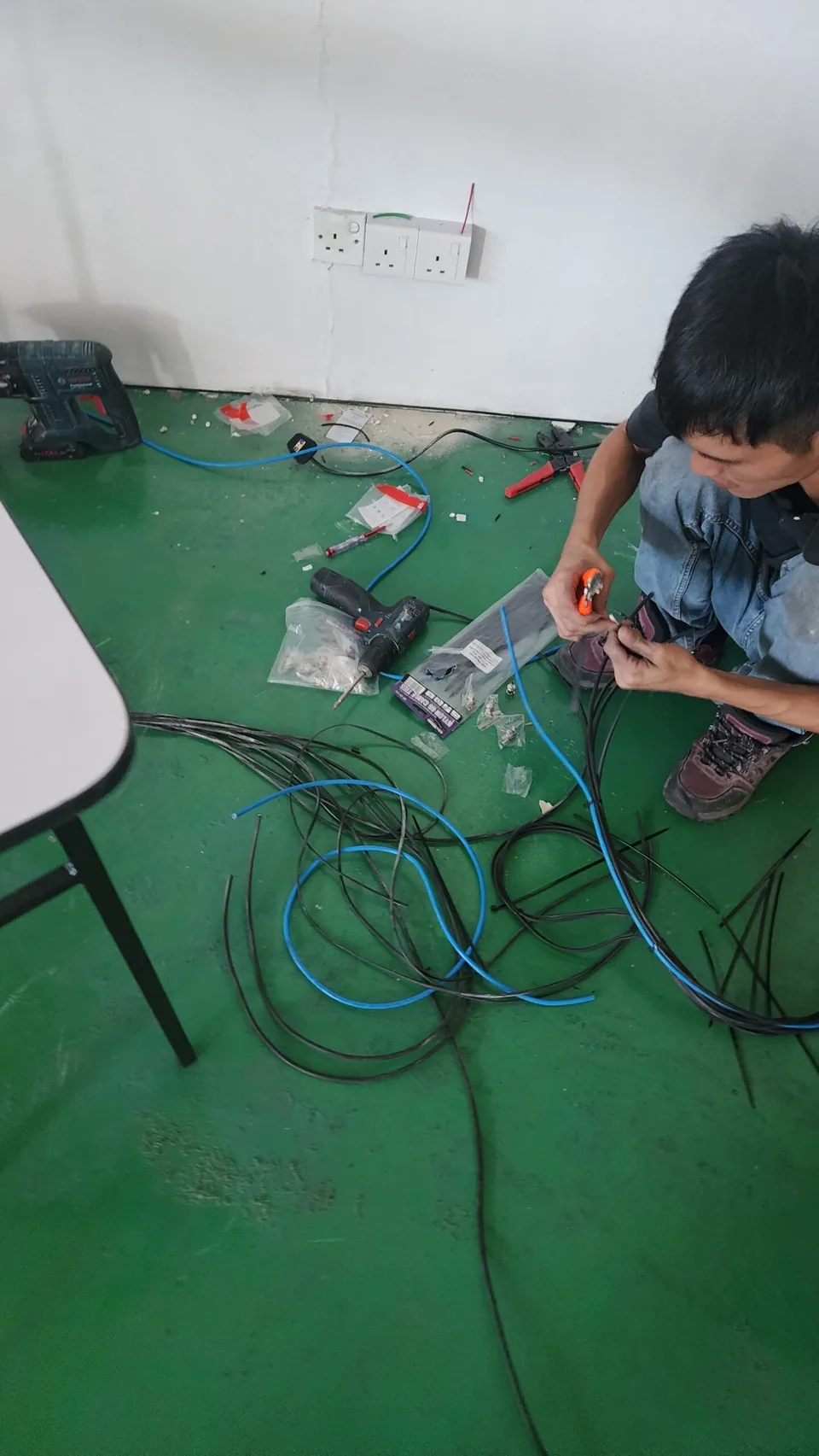 Technician sorts coiled cable and tools on a workshop floor.